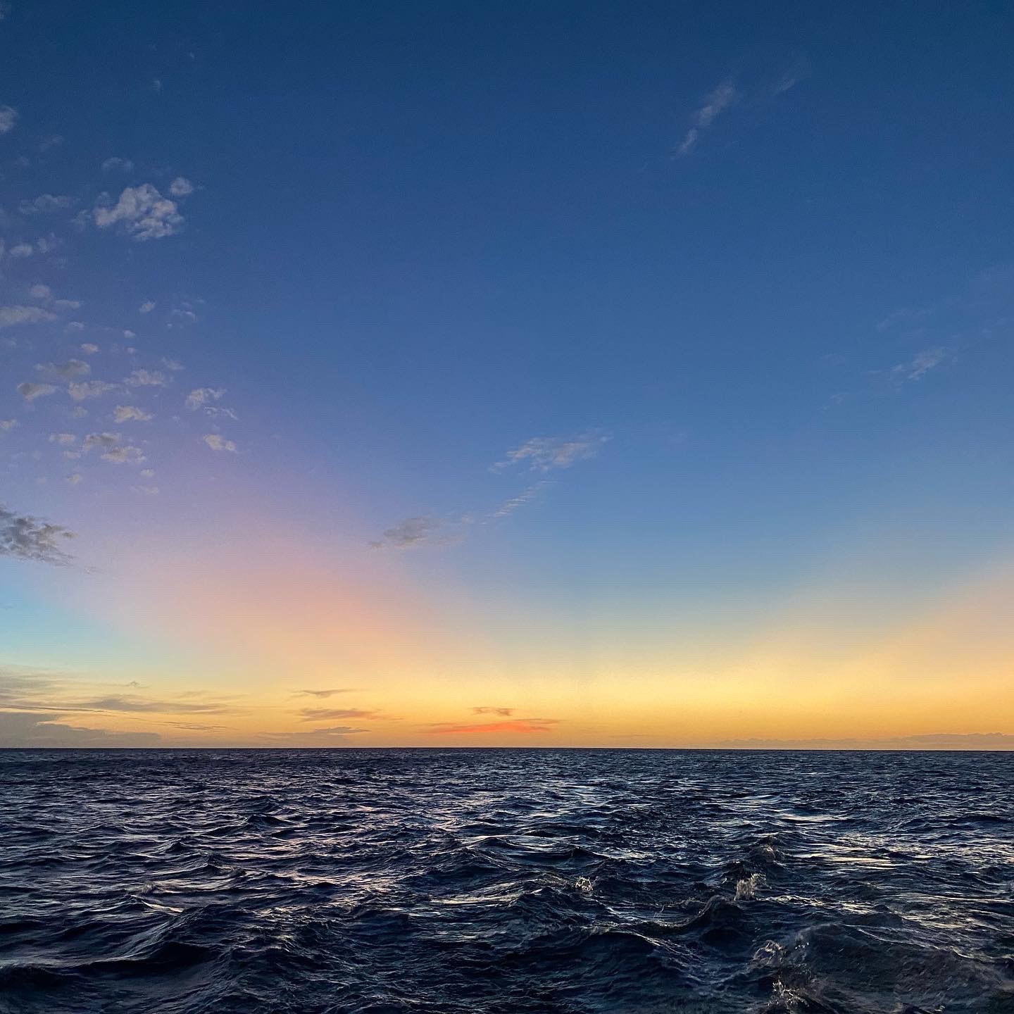 A sunset on the water in Hawaii. The horizon is bright yellow, and above that, rays of orange, all of it against an almost cloudless blue sky. 