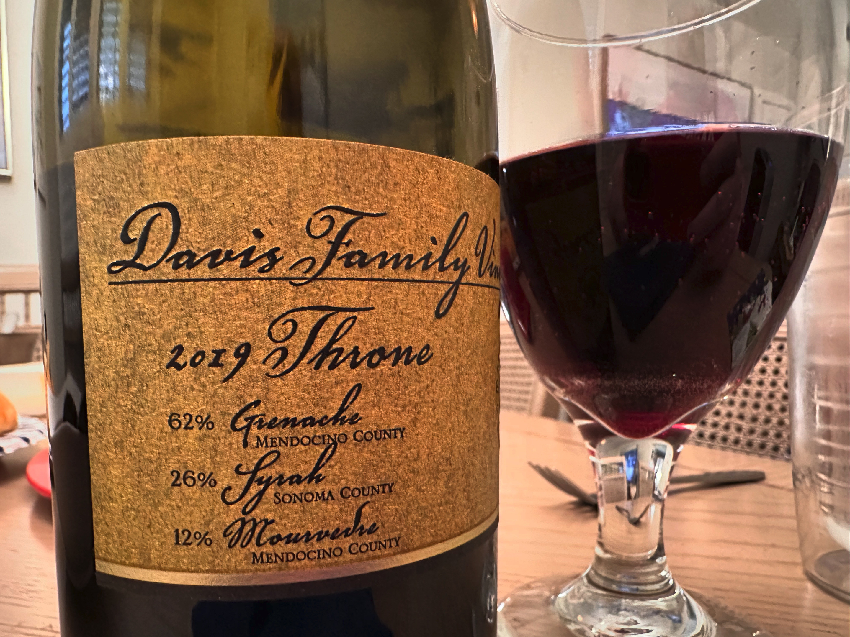 A bottle of Davis Family Vineyards 2019 Throne next to a wine glass half full of the wine. 